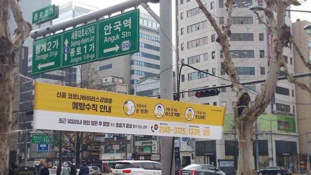 1Coronavirus Vorbeugungsempfehlungen auf Straßenbanner in Jongno / Seoulam .0.00; © Bonnielou013 / Wikimedia Commons CC BY-SA 4.0