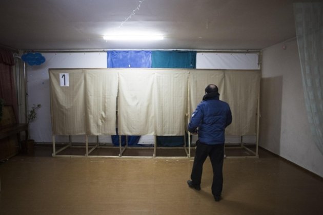 Wahllokal im Ort Dobroe nahe Simferopol. Ein Milizionär der prorussischen Selbstverteidigungskräftekontrolliert die Wahlkabinen Foto: AP